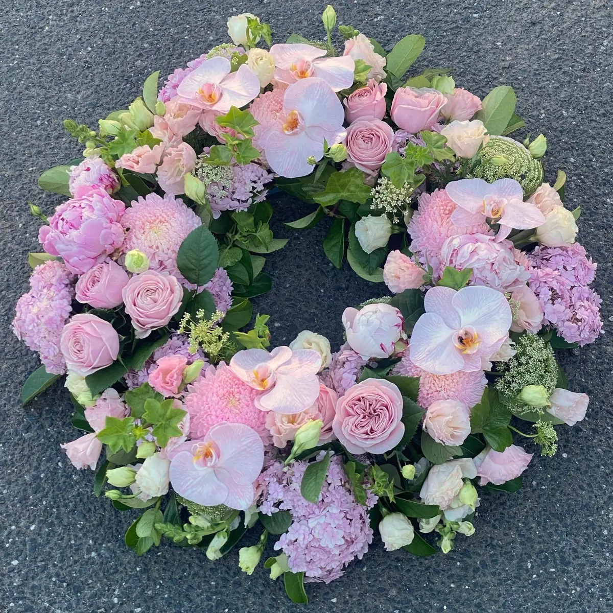 Classic round funeral wreath of soft pink orchids, roses and peonies